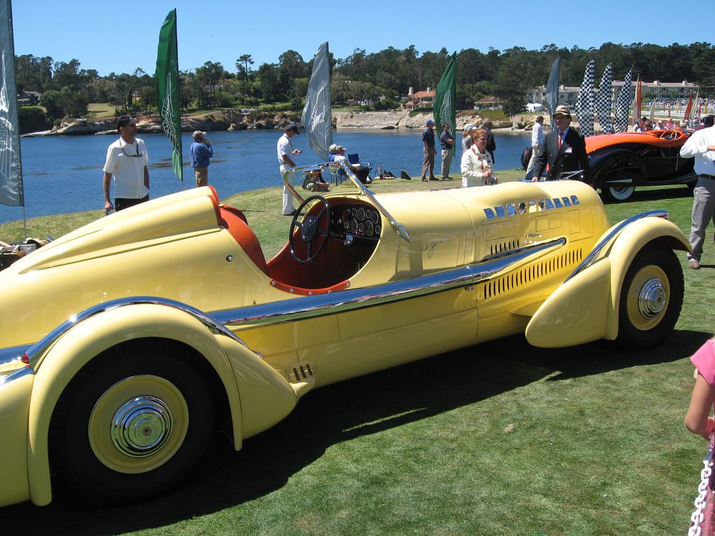 Duesenberg SJ amarillo tipo speedster sobre el césped de Pebble Beach, con el mar de fondo.