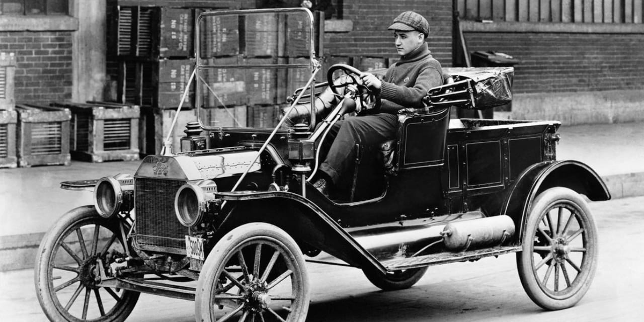 Fotografía en blanco y negro de un Ford Modelo T de hacia 1910 con su placa numerada al frente.